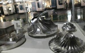 High-precision 5-axis machined metal parts displayed on a glass surface.
