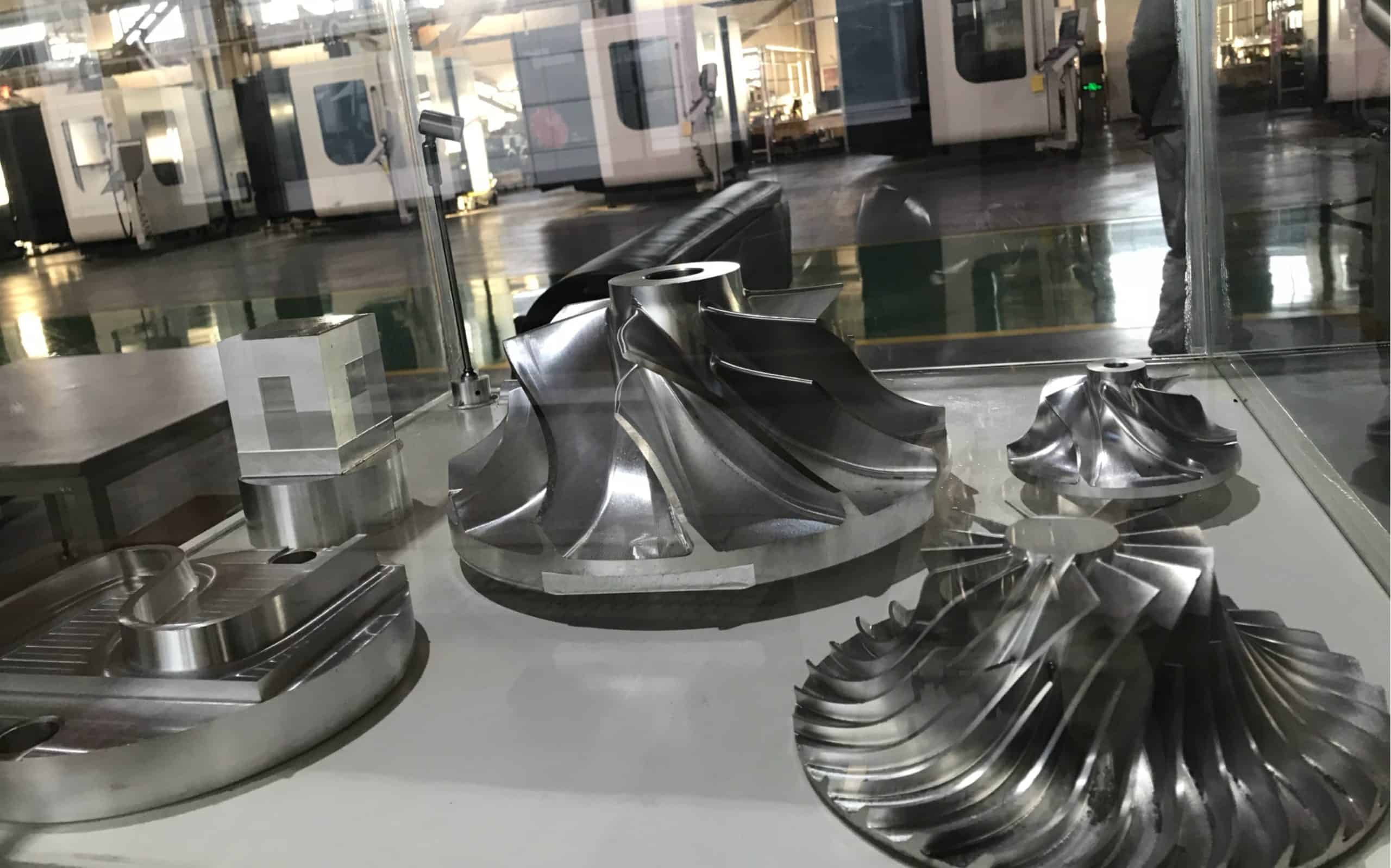 High-precision 5-axis machined metal parts displayed on a glass surface.
