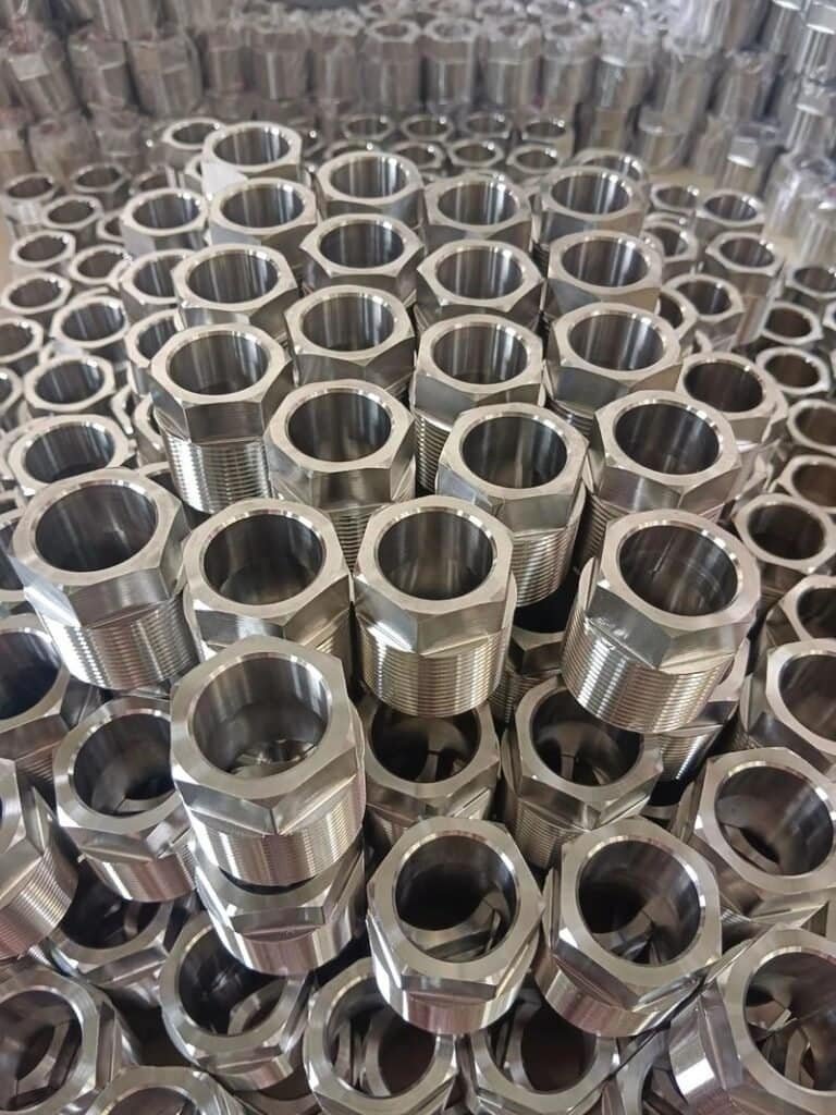 Aluminum CNC machined hexagonal nuts arranged in a pile for manufacturing.